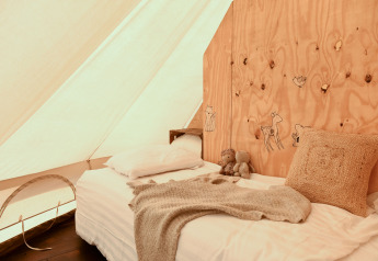 Gemütliches Bett in einem Smûk Grutte Bell Zelt, dekoriert mit Holzwand und Kuscheldecke.