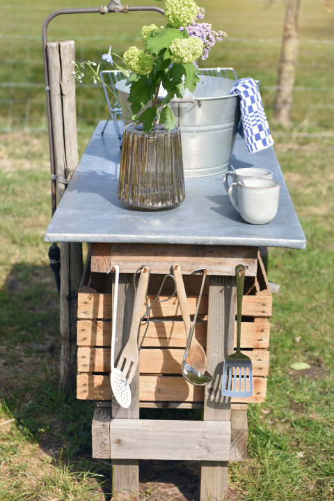 Buitenkeuken bij een safaritent met bloemen, metalen emmer, mokken en keukengerei aan de haak in Nederland.