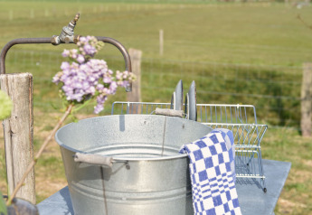 Outdoor-Spülstation mit Metalleimer und blauem Geschirrtuch bei Smûk Grutte Bell Tent, Niederlande.