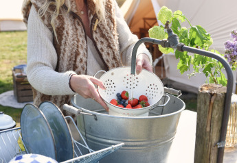 Eine Person wäscht Beeren in einem Sieb unter einem Wasserhahn bei einem Safarizelt in den Niederlanden.