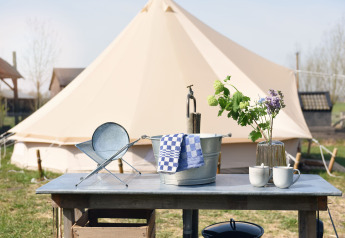 Buitentafel met metalen emmer, kopjes en bloemen voor een safaritent bij Smûk Recreatie in Nederland.
