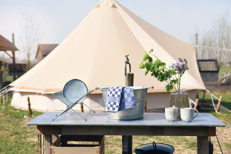 Outdoor-Tisch mit Metalleimer, Tassen und Blumen vor einem Safari-Zelt bei Smûk Recreatie in den Niederlanden.
