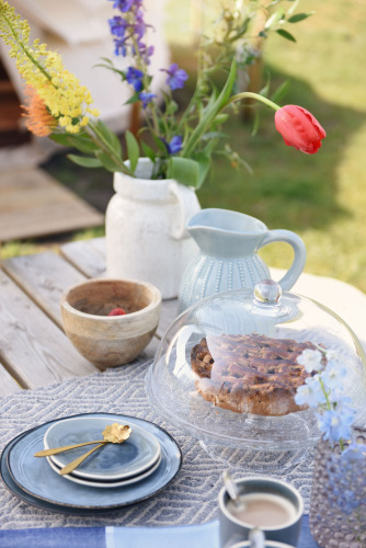 Rustikaler Kaffe- und Kuchentisch mit Blumen und Kuchen im Glasdom bei Smûk Grutte Bell Tent in den Niederlanden.