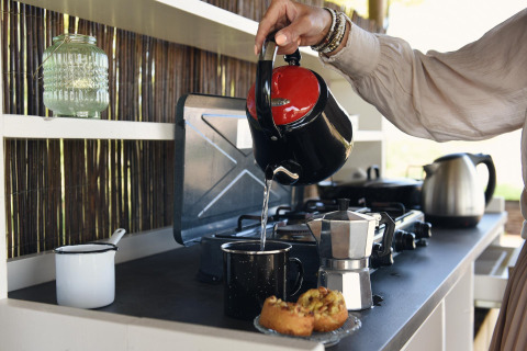 Person pours hot water from a kettle into a mug on a kitchen counter with pastries in Friesland, Netherlands.