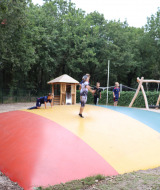 Des enfants jouent sur un grand coussin sauteur coloré au Holiday Park Duinhoeve, entourés d’arbres verts.