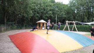 Niños jugando en una gran almohadilla de salto colorida en Holiday Park Duinhoeve, rodeados de árboles.