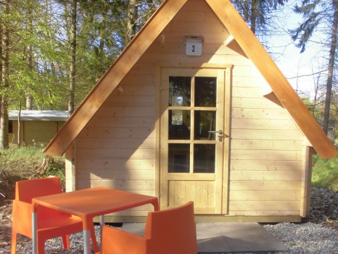Kleine Holzhütte mit orangefarbenen Stühlen und Tisch, gelegen im Waldpark Vakantiepark 't Urkerbos, Niederlande.