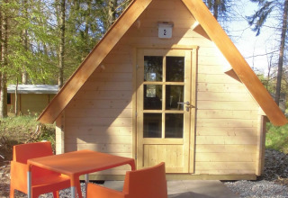 Kleine houten lodge met oranje stoelen en tafel bij Vakantiepark 't Urkerbos in Nederland.