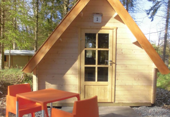 Lille træhytte med orange stole og bord foran, beliggende i skov ved Vakantiepark 't Urkerbos i Holland.