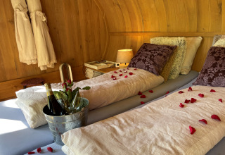 Dormitorio romántico en Boomhut Suite con pétalos de rosa, champán y cojines en Buytenplaets Suydersee.