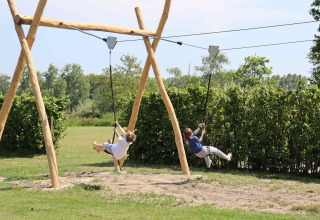 To børn leger på svævebane i en grøn park med træramme på Holiday Park Duinhoeve, Nord-Brabant, Holland.