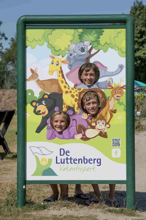 Tres niños posan en un cartel de animales de dibujos en Vakantiepark De Luttenberg, Países Bajos.