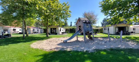 Parque infantil con tobogán y zona de arena, rodeado de casas de vacaciones en De Luttenberg, Overijssel.