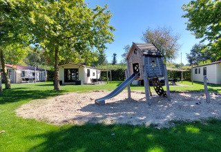 Speeltuin met glijbaan en zandbak, omringd door vakantiehuisjes in vakantiepark De Luttenberg, Overijssel.