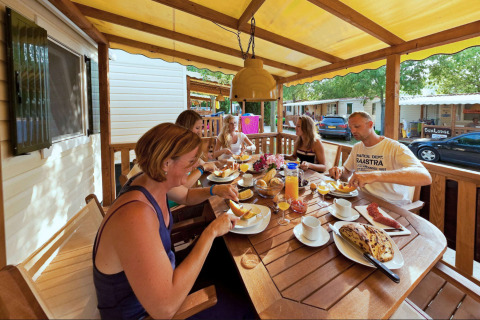 Famiglia fa colazione sul terrazzo in legno della SunLodge Maple al Camping Bella Italia, in Italia.