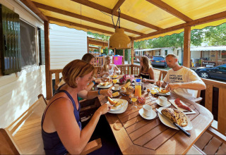 Gezin geniet van ontbijt op het houten terras van SunLodge Maple bij Camping Bella Italia, Italië.