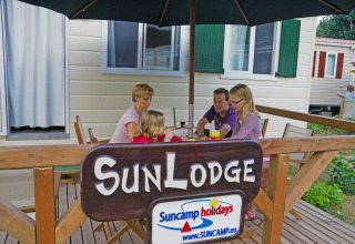 Gezin geniet op het terras van SunLodge Maple aan Camping Bella Italia, Italië, onder een parasol.