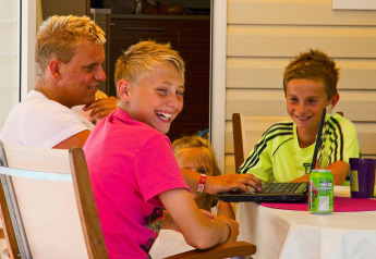 Cuatro niños se divierten juntos en una mesa con un portátil en SunLodge Maple, Camping Bella Italia.