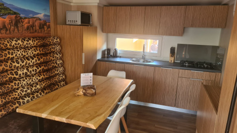 Cucina moderna e zona pranzo al SunLodge Babul con arredamento in legno, seduta leopardata e arte safari.
