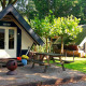 Dos pequeñas casas Trekkershut en un entorno boscoso, con mesa de picnic y chimenea al aire libre.