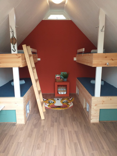 Kleine hut met vier stapelbedden, houten interieur en een kleurrijk tijgertapijt op de vloer.