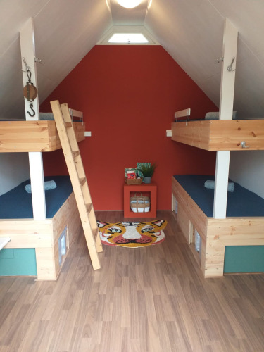 Petite chambre avec quatre lits superposés, intérieur en bois et tapis tigre coloré sur le sol.