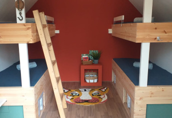Vier Etagenbetten in einer kleinen, modernen Holzhütte mit roter Wand und buntem Tigerteppich am Boden.