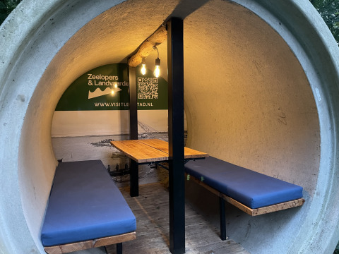 Interior de una cabaña redonda de hormigón con bancos y mesa en Kajuitboot, Buytenplaets Suydersee, Países Bajos.