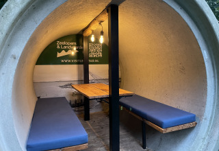 Interior de una cabaña redonda de hormigón con bancos y mesa en Kajuitboot, Buytenplaets Suydersee, Países Bajos.