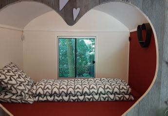 Gemütliches Zimmer mit herzförmiger Öffnung, Einzelbett und Blick ins Grüne durch das Fenster.