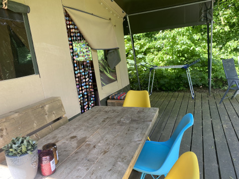 Terrasse extérieure d'une tente safari à Buytenplaets Suydersee avec table en bois, chaises colorées et plantes.