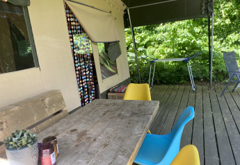 Outdoor terrace of a safari tent at Buytenplaets Suydersee featuring a wooden table, colorful chairs, and plants.