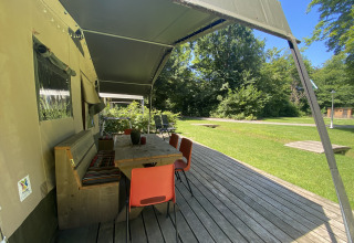 Terraza cubierta con mesa de madera y sillas junto a tienda safari en Buytenplaets Suydersee, Países Bajos.