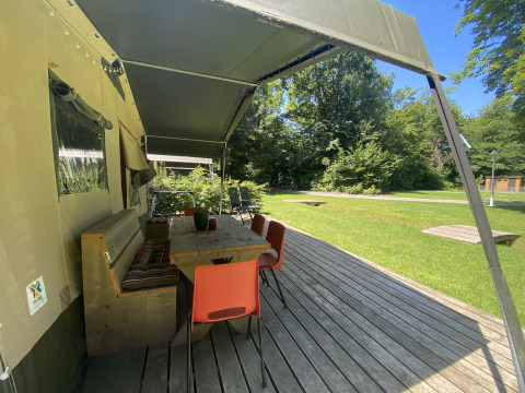 Terrasse en bois couverte avec table et chaises devant une tente safari à Buytenplaets Suydersee, Pays-Bas.