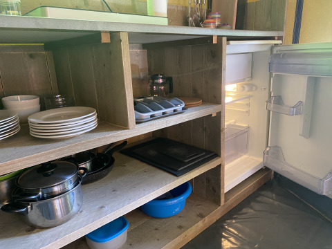 Kitchen area in Safari tent at Buytenplaets Suydersee, Netherlands, with open fridge and kitchen utensils.