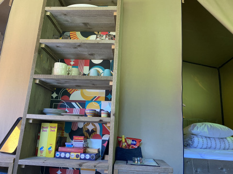 Scaffale da cucina con stoviglie, lattine di Donald Duck e giochi in tenda safari a Buytenplaets Suydersee, Olanda.