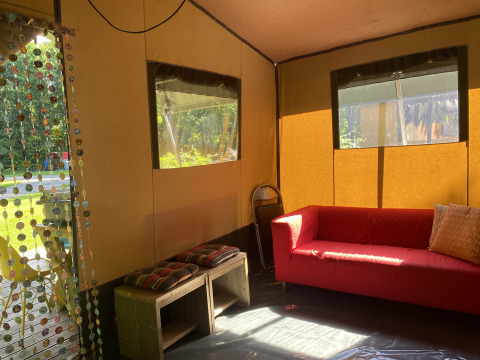 Intérieur d’une tente safari à Buytenplaets Suydersee, Pays-Bas, avec un canapé rouge et des bancs en bois.