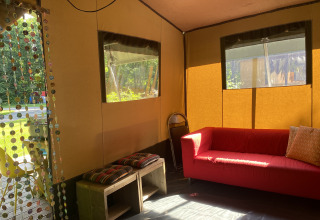 Intérieur d’une tente safari à Buytenplaets Suydersee, Pays-Bas, avec un canapé rouge et des bancs en bois.