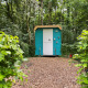 Kleines blaues Haus namens Pipo Pip im Wald, umgeben von Bäumen und grünen Sträuchern auf Waldboden.