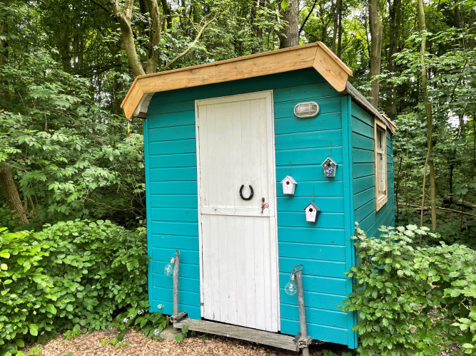 Ein kleines türkisfarbenes Haus mit weißer Tür im Wald bei Buytenplaets Suydersee, Niederlande.