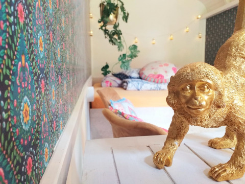 Habitación colorida con papel tapiz floral, estatua de mono dorada y cama acogedora al fondo.