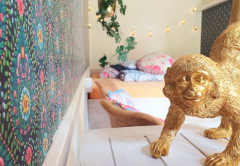 Habitación colorida con papel tapiz floral, estatua de mono dorada y cama acogedora al fondo.