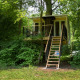 Modern treehouse named Boomhut Family elevated among lush green trees with a wooden staircase leading up.