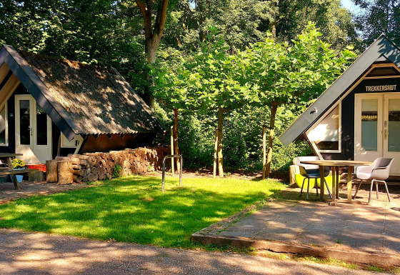 Deux petites cabanes boisées, dont une nommée 'Trekkershut', avec tables, chaises et verdure autour.