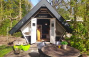 Pequeña casa triangular Trekkershut en Buytenplaets Suydersee, Países Bajos, rodeada de árboles y naturaleza.