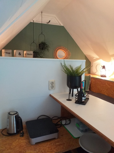 Rincón acogedor en el ático de una tiny house llamada Trekkershut, con escritorio, plantas y tetera en Holanda.