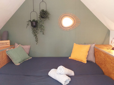 Cozy bed area in a tiny house Trekkershut at Buytenplaets Suydersee, Netherlands, with pillows and plants.