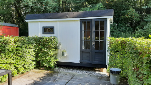 Kleines weißes Lodge namens Pipo Maison bei Buytenplaets Suydersee in den Niederlanden, umgeben von Hecken.