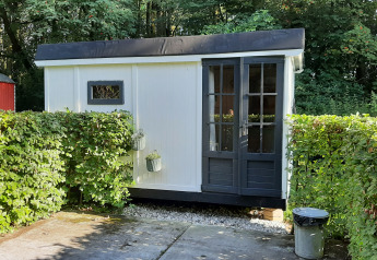 Klein wit lodgehuisje, Pipo Maison genoemd, bij Buytenplaets Suydersee in Nederland, omringd door groene hagen.