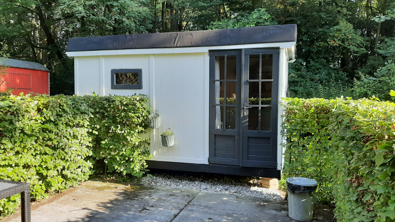 Pequeño albergue blanco llamado Pipo Maison en Buytenplaets Suydersee, Países Bajos, con setos verdes alrededor.